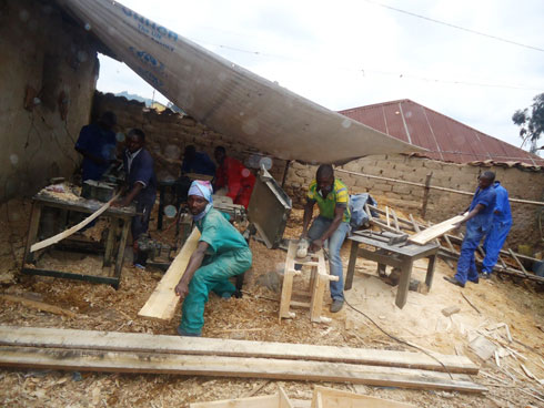 Niyibizi Emmanuel wambaye isarubeti y'icyatsi n'abakozi be ku mamashini mu kazi gatandukanye k'ububaji.