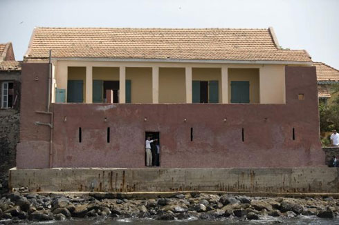 Obama (ibumoso), ahagararanye n'ushinzwe inzu ndangamurage y'ubucakara Eloi Coly (iburyo). Barimo kureba inyanja abirabura banyuzwagamo mu mato nyuma yo kunyura mu muryango w'ubutagaruka 'DOOR OF NO RETURN' ku kirwa cya Goree.