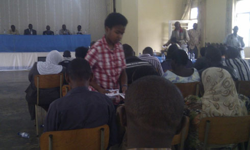 Umwe mu bana ba kandida Kansanga atanga impapuro zamamaza umubyeyi we mu baturage.