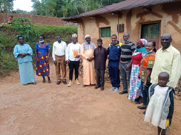 Umusaza Mitima (wambaye ingofero y'umukara) hagati y'abanyeshuri yigishije guhera mu 1985 imbere y'inzi ishaje yabagamo