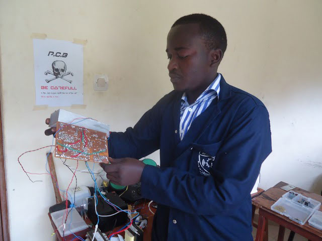 Kazungu Robert yerekana plaquette yakoze. Aha amaze kuyishyiraho insinga zizatuma ibasha gukorana n'ibindi bikoresho.