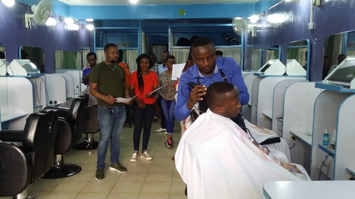 Uwogosha ari mu kizamini, Abamuhagaze inyuma bafite impapuro ni abatanga amanota